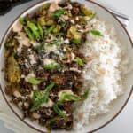 ground beef and brussels sprouts in a bowl with white rice garnished with scallions, cotija cheese, and spicy crema