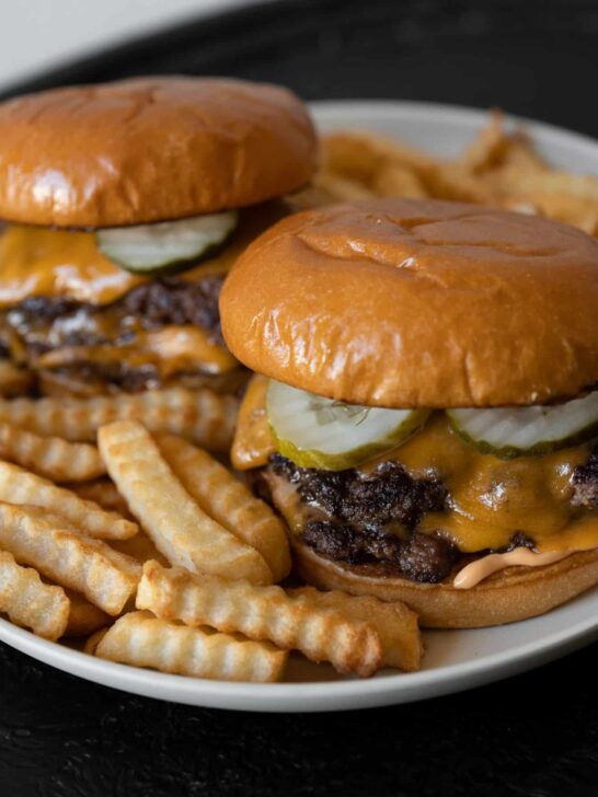 two bison cheeseburgers on a plate with crinkle cut fries