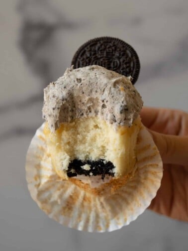 A vanilla cupcake with an Oreo baked into the bottom, that has a bite taken out of it to show the Oreo.