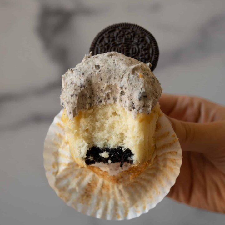 A vanilla cupcake with an Oreo baked into the bottom, that has a bite taken out of it to show the Oreo.