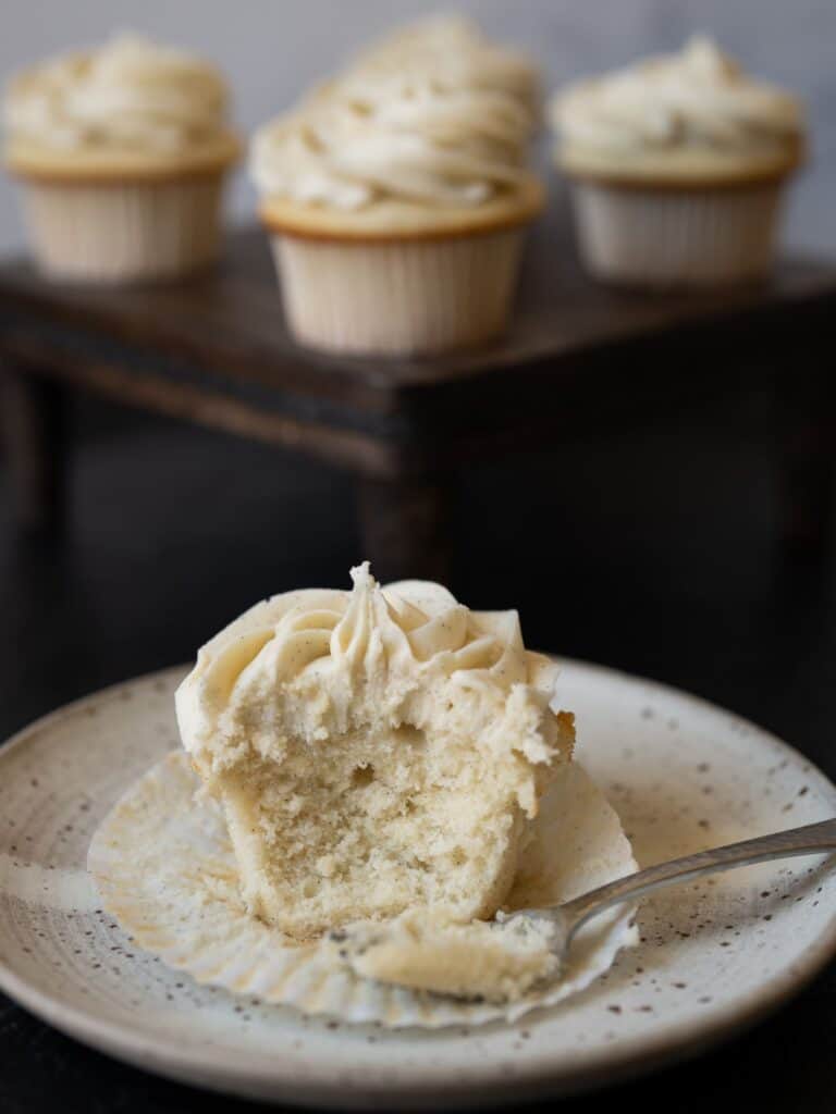 A vanilla bean cupcake with a bite taken out with a fork.