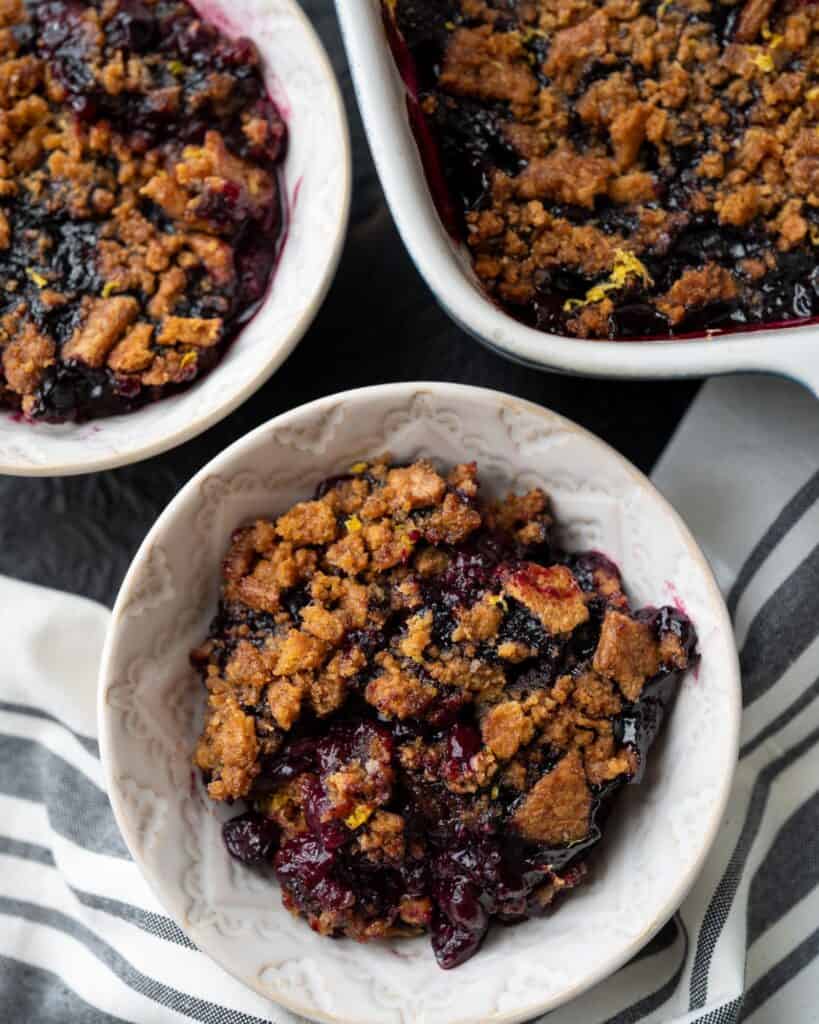 two bowls of smoked blueberry crisp beside a baking dish
