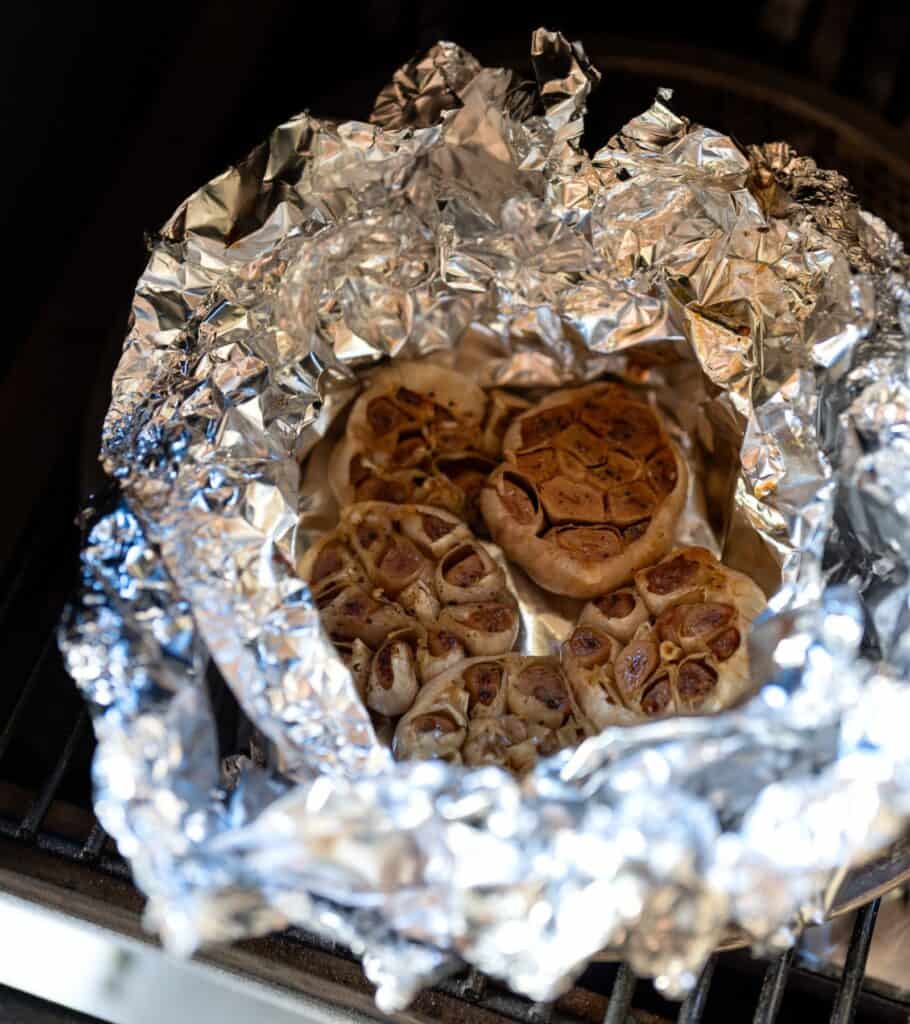 roasted garlic bulbs wrapped in foil on a Traeger grill