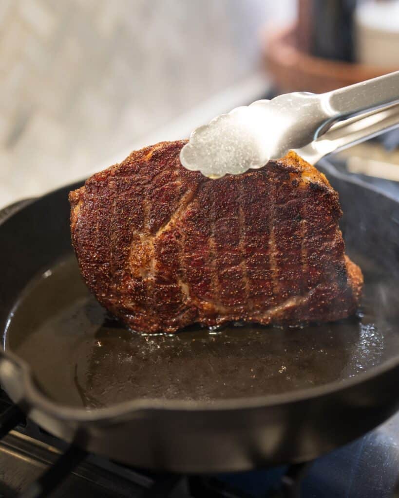 using tongs to sear a smoked ribeye steak in a cast iron skillet