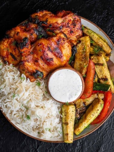 Traeger grilled chicken thighs and veggies in a bowl with basmati rice and tzatziki sauce