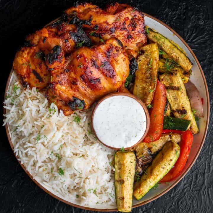 Traeger grilled chicken thighs and veggies in a bowl with basmati rice and tzatziki sauce