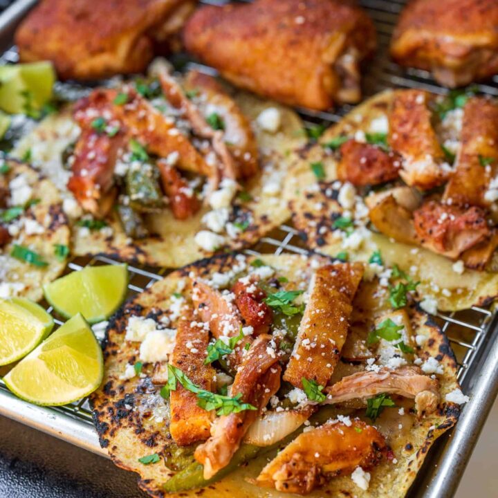 smoked chicken tacos with peppers and onions on a sheet pan garnished with cilantro, cotija cheese, and lime wedges