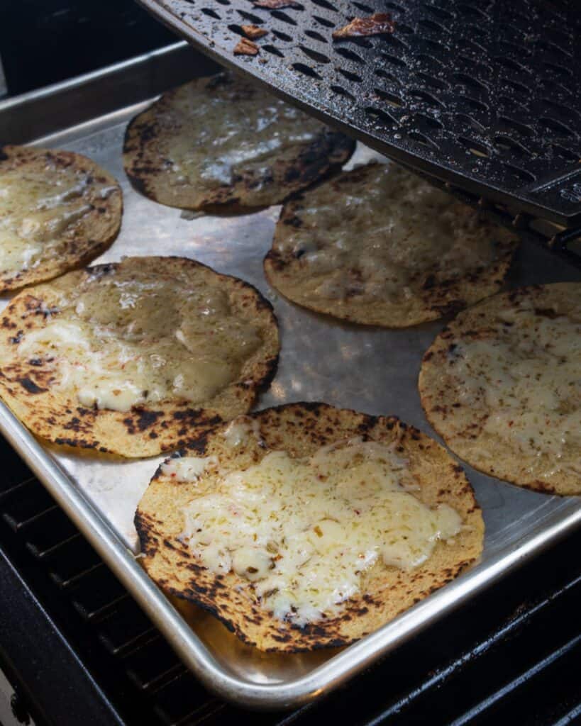 charred tortillas topped with cheese on a sheet pan inside the grill