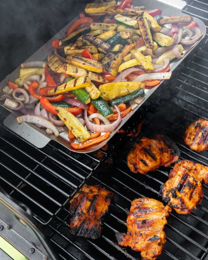 grilled chicken thighs on a Traeger with grilled veggies on a grill pan on the top rack