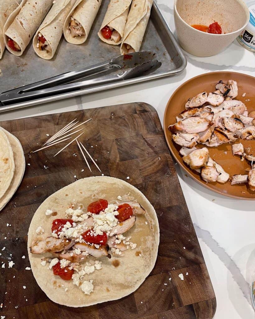 rolling sliced grilled chicken, crumbled feta cheese, and roasted tomatoes in flour tortillas