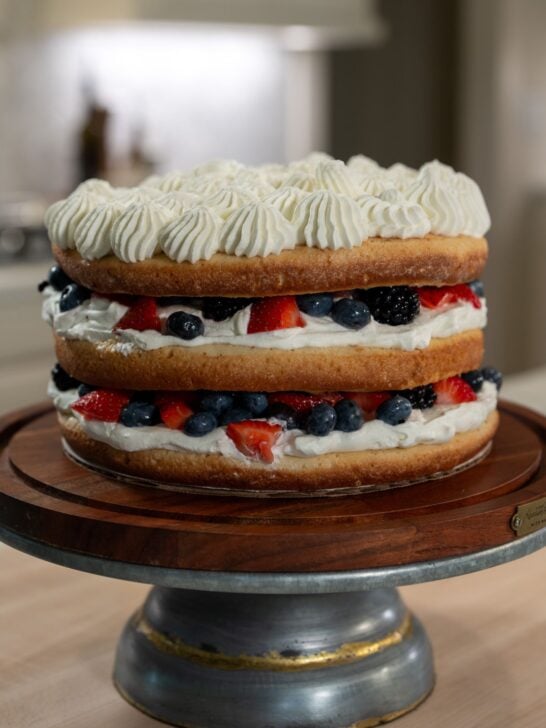 Three layer milk and berries cake with a sponge cake layer, a whipped cream layer, and a summer berries layer.