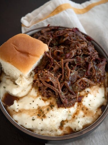 smoked pot roast in a bowl with mashed potatoes and a roll